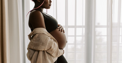 Pregnant woman holding her belly, looking out the window.